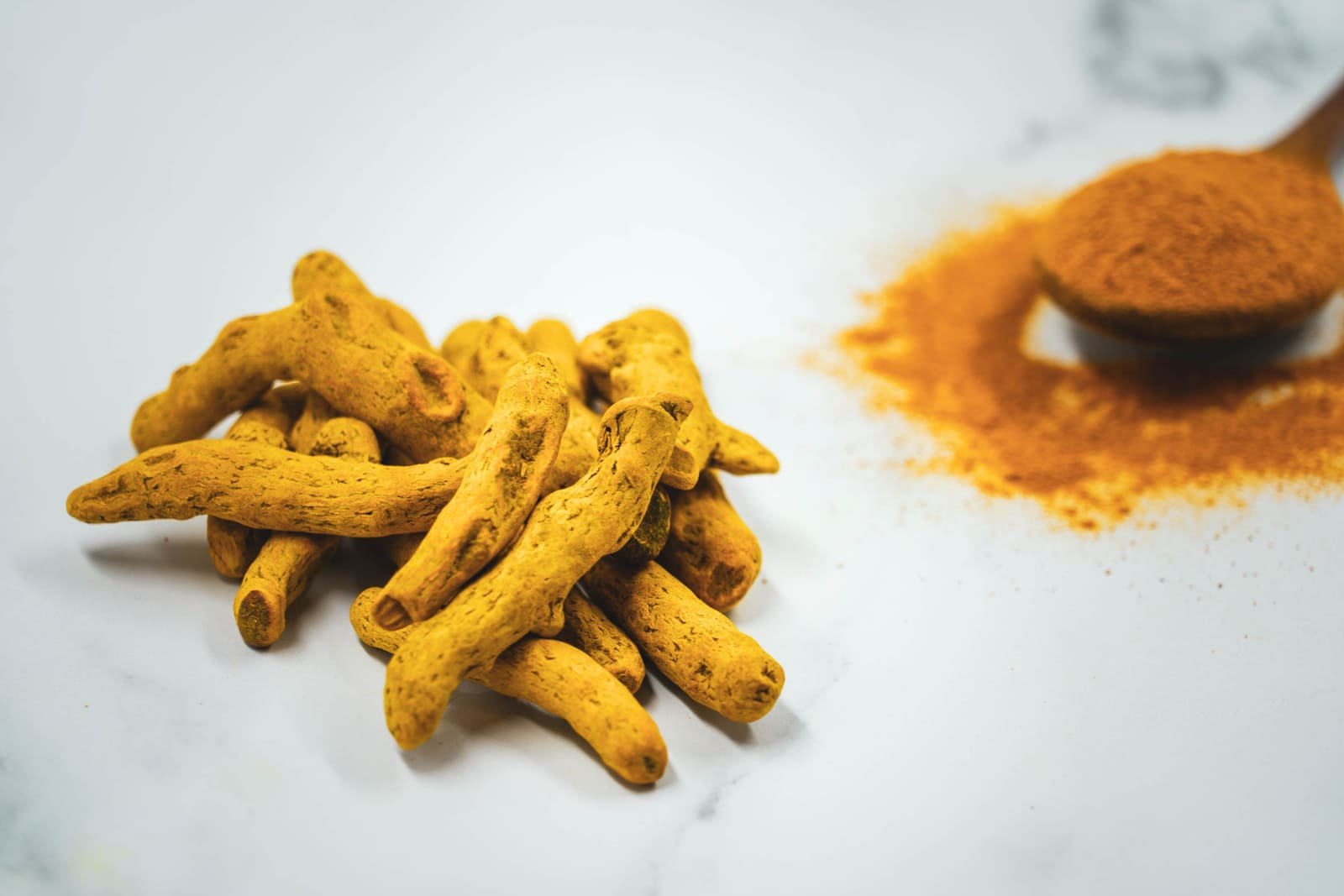Rizomas e pó de cúrcuma (Curcuma longa) sobre superfície clara.