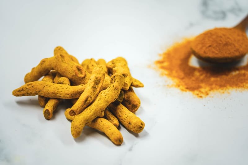 Rizomas e pó de cúrcuma (Curcuma longa) sobre superfície clara.